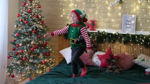 Little cheerful boy in an elf hat jumps on the bed holding his mother's hands Stock Footage 165389986