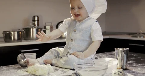 The little chef cook is sitting on the table and rolling out the dough. Stock Footage 85812636