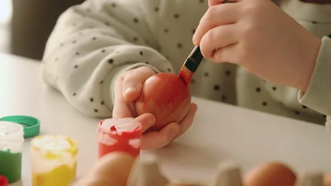 Little child decorates Easter eggs with colored red food paint. Stock Footage 168819966