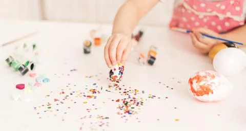 Little Child decorates Easter eggs with glitter Stock Photos