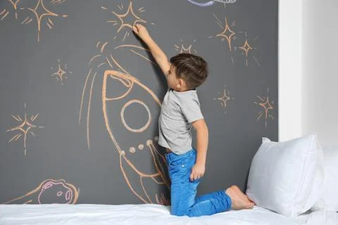 Little child drawing rocket with chalk on wall in bedroom Stock Photos