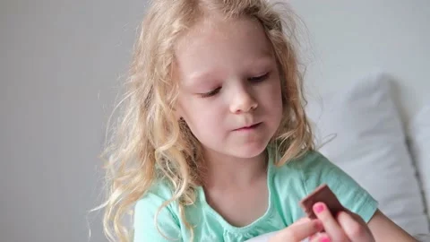 Little child eats chocolate on the white bed. the pleasure of eating sweets Stock Footage 197580147