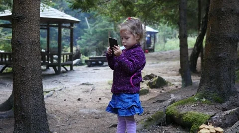 Little child girl stay in forest nature park type slide watch smart phone game Stock Footage