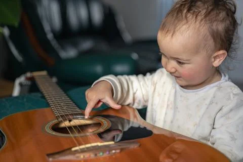 Little child learning guitar strings at home in cozy environment. Child pla.. Stock-Fotos