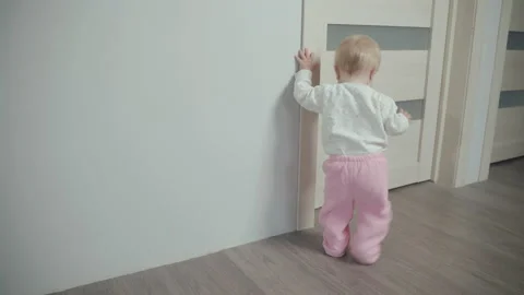 Little Child Learns Walking Take First Steps Holding Wall Hand At Home Stock Footage 142279231