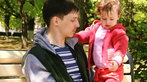 Little child puts on pulls a red hat on his head. two year old kid girl and dad Stock Footage 90265171