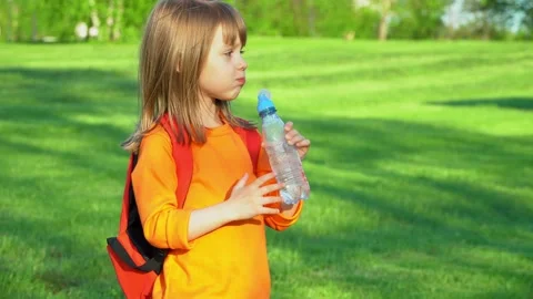 Little child with school backpack drinks water from bottle in summer park. Stock Footage 154356990