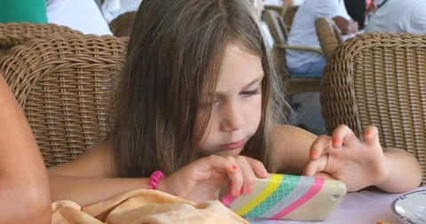 Little child using smartphone sitting on chair of restaurant on summertime Stock Footage 118260289