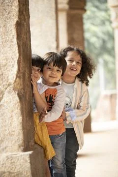 Little Children Posing In Front Of Camera While Standing Behind Ancient Column 스톡 사진