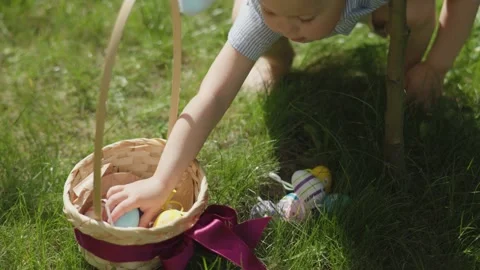 Little child's hands picking up Easter eggs basket outdoors from green grass Stock Footage 234931187
