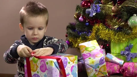 Little curious boy sitting under the Christmas tree unties the ribbon on the Stockbeeldmateriaal 163090954