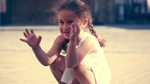 A little curly-haired girl laughing at the little sea shell and playing with it Stock Footage