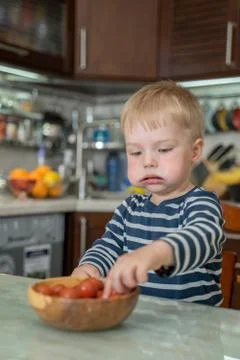 Little cute blond boy eats fresh juicy red cherry tomatoes with pleasure and  Stock Photos