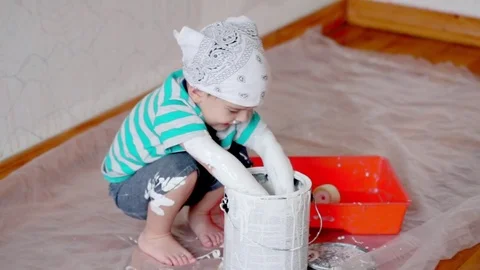 Little cute boy kid dunks hands in paint can painting wall at home Stock Footage 71074015