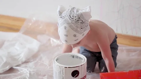 Little cute boy kid dunks finger in paint can painting wall at home Stock Footage 71074173