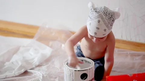 Little cute boy kid dunks finger in paint can painting wall at home Stock Footage 71074410