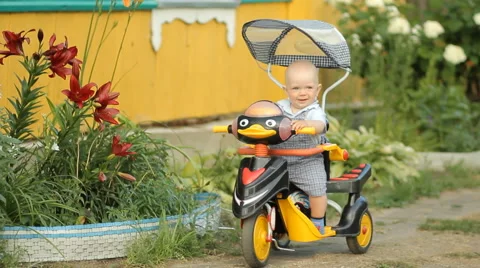 Little cute boy sitting in a stroller bike and smiles near the country house Stock Footage 64998477