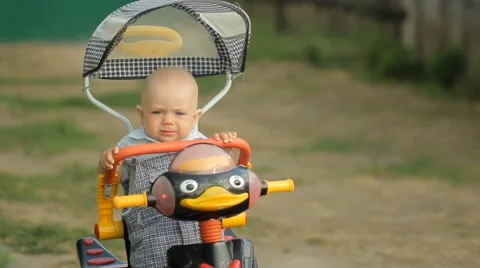 Little cute boy sitting in a stroller bike and smiles near the country house Stock Footage 64998702