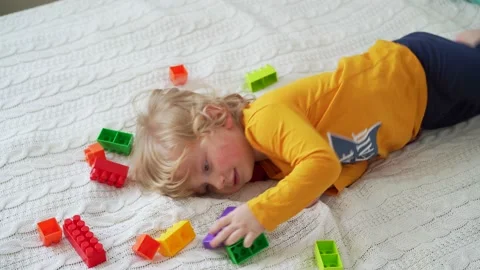 Little cute boy of two years old plays children's constructor sitting on the bed Stock Footage 169543706