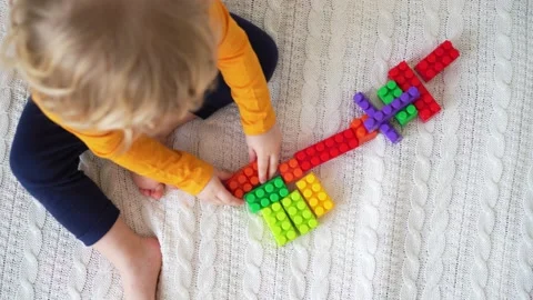 Little cute boy of two years old plays children's constructor sitting on the bed 스톡 동영상 169543834
