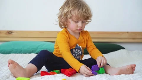 Little cute boy of two years old plays children's constructor sitting on the bed Stock Footage 169543987
