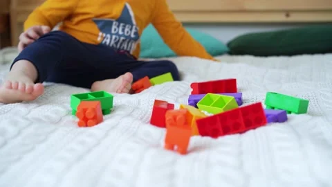 Little cute boy of two years old plays children's constructor sitting on the bed Stock Footage 169544217