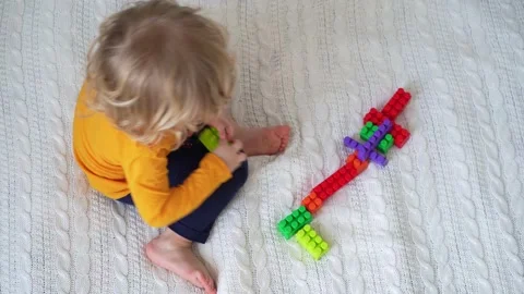 Little cute boy of two years old plays children's constructor sitting on the bed Stock Footage 169544244