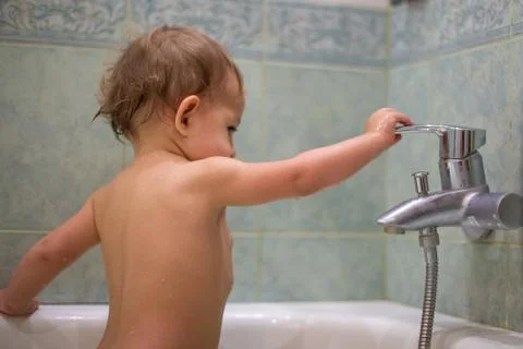 A little cute child, while bathing in the bath, plays with a water tap, turns Stock Photos
