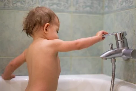 A little cute child, while bathing in the bath, plays with a water tap, turns it Stock Photos