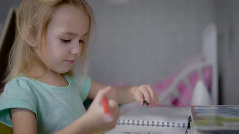 Little cute girl with blond hair, wearing a blue t-shirt sitting at the table Stock Footage