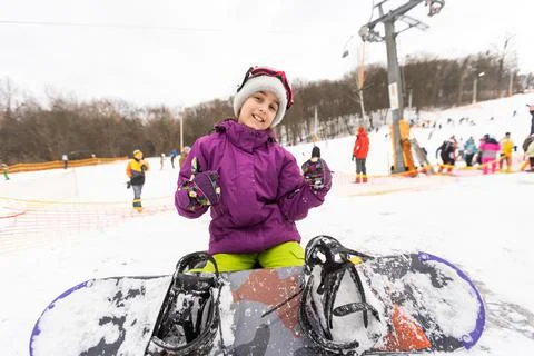 Little cute girl learning to ride a children's snowboard, winter sports for the Stock Photos