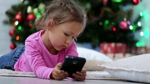 Little cute girl using smart phone, in front of Christmas tree. Close-up shot. Stock Footage