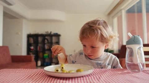 Little cute kid with appetite eats olives itself with fork Stock Footage 229479413