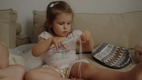 Little daughter playing with strings for threading activity on the sofa indoors Stock Footage 256924255