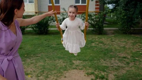 Little daughter waves hand to camera playing swings with mother on playground Stock Footage 246947293