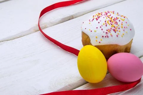 Little easter cake and colored easter eggs with red ribbon on white wooden ba Stock Photos