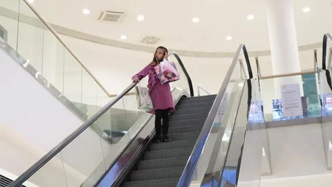 A little fashionista with packages in a large shopping center rides down an Stock Footage