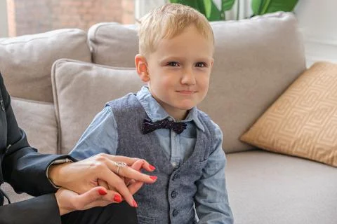 Little five-year-old boy in a shirt with a bow tie sits on the couch and hold Stockfoto's