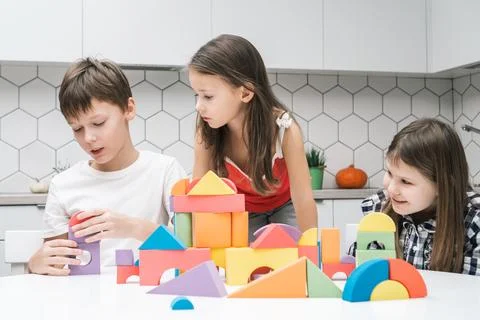 Little friends play constructor on table. Girls look at boy collect colorful Stock Photos