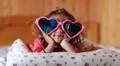 Little girl in big glasses in the shape of hearts lies on the bed HD Footage