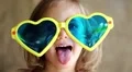 Little girl in big sunglasses in the shape of hearts looks at the camera HD Footage