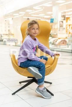 Little girl in a blue jumper sitting in a yellow chair Stock Photos