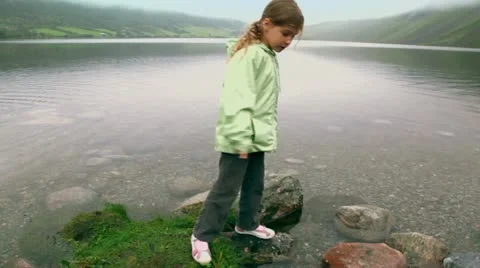 Little girl checks stone in water of fiord with mountains Stock Footage