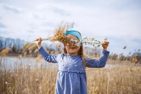 Little girl child holds dry reeds and a branch with small white flowers in ha Stock Photos