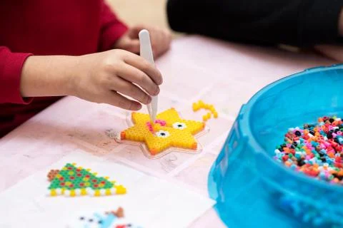 Little girl creates pattern using perler beads. Fusible colorful beads. Toy Fotos Stock