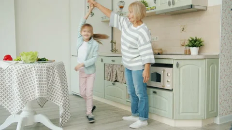 Little girl dancing with grandmother in kitchen, elderly woman showing thumbs-up Stock Footage 133595475