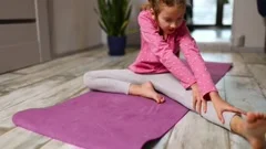 Fotografia do Stock: Little girl doing stretching exercises, practicing yoga  on fitness mat at home