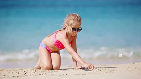 Little girl drawing pictures on sandy beach Stock Footage