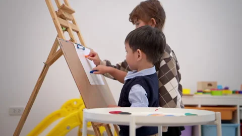 Little girl drawing while a boy walks around, reflecting independent activities Stock Footage 339565495