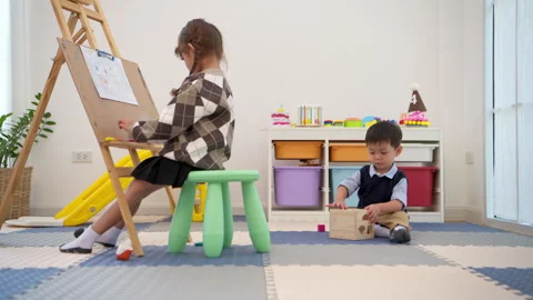 Little girl drawing while a boy walks around, reflecting independent activities Stock Footage 339567971